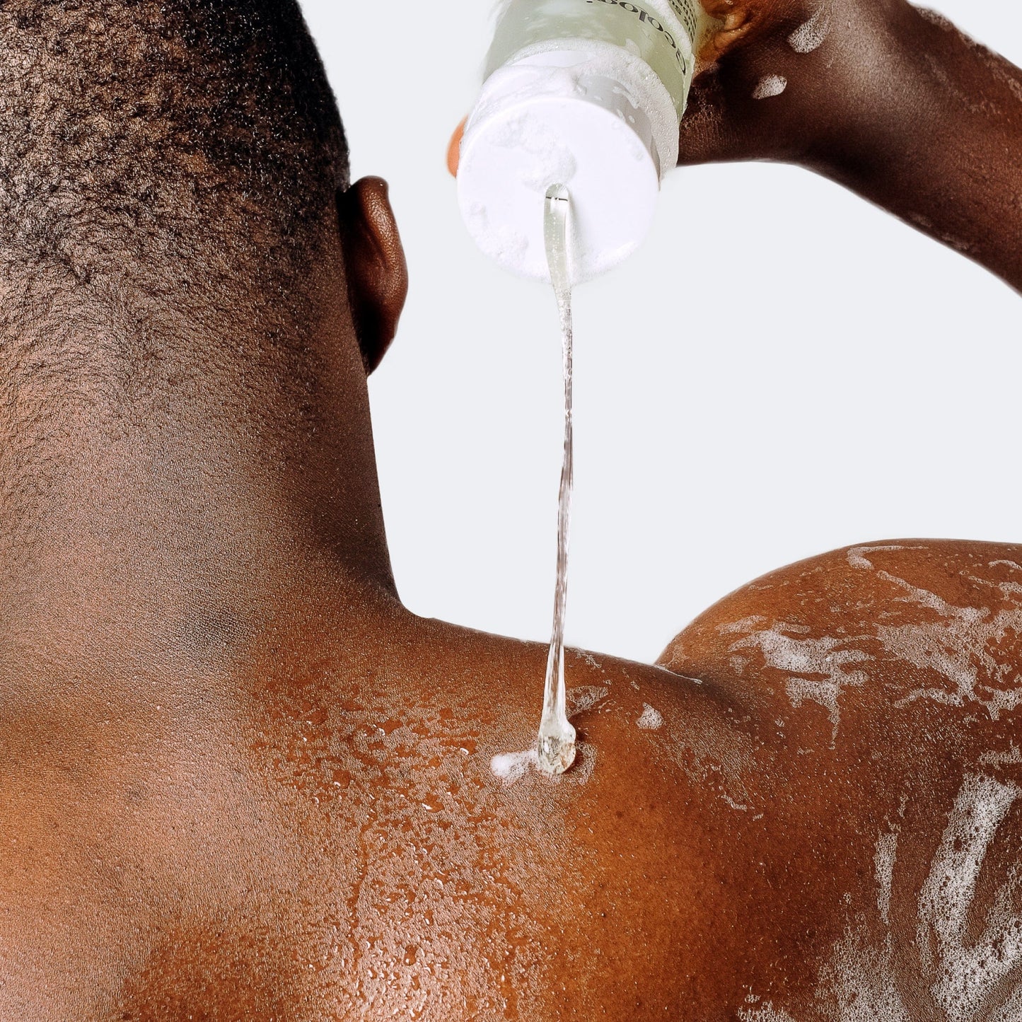 Person applying Acne Body Wash to their back from a bottle.