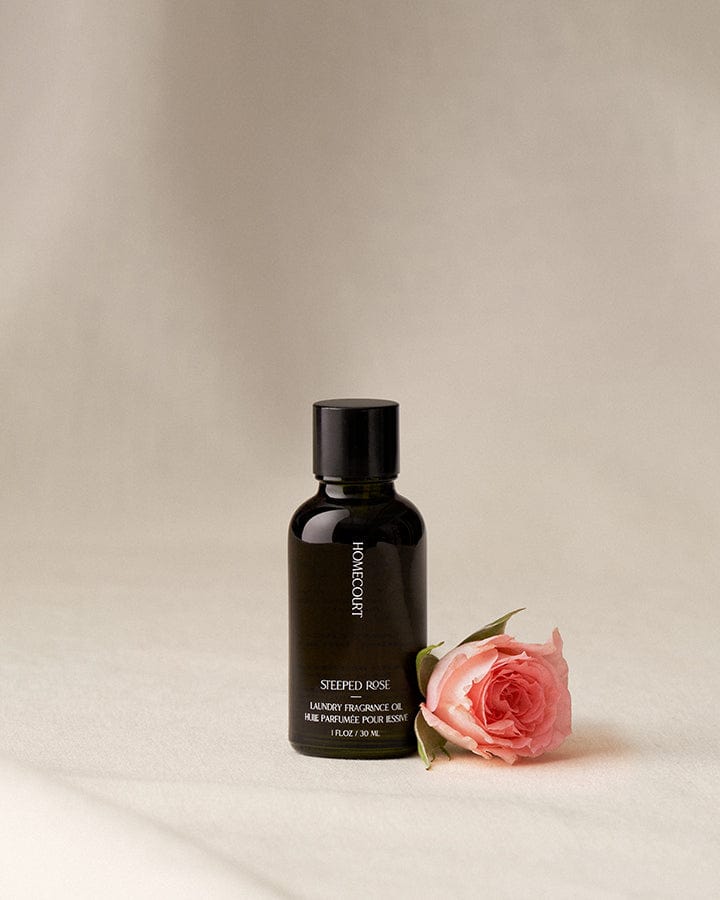 Black bottle of Steeped Rose Scented Fragrance Refill for Dryer Balls on a beige background with Neroli fruit and leaves.