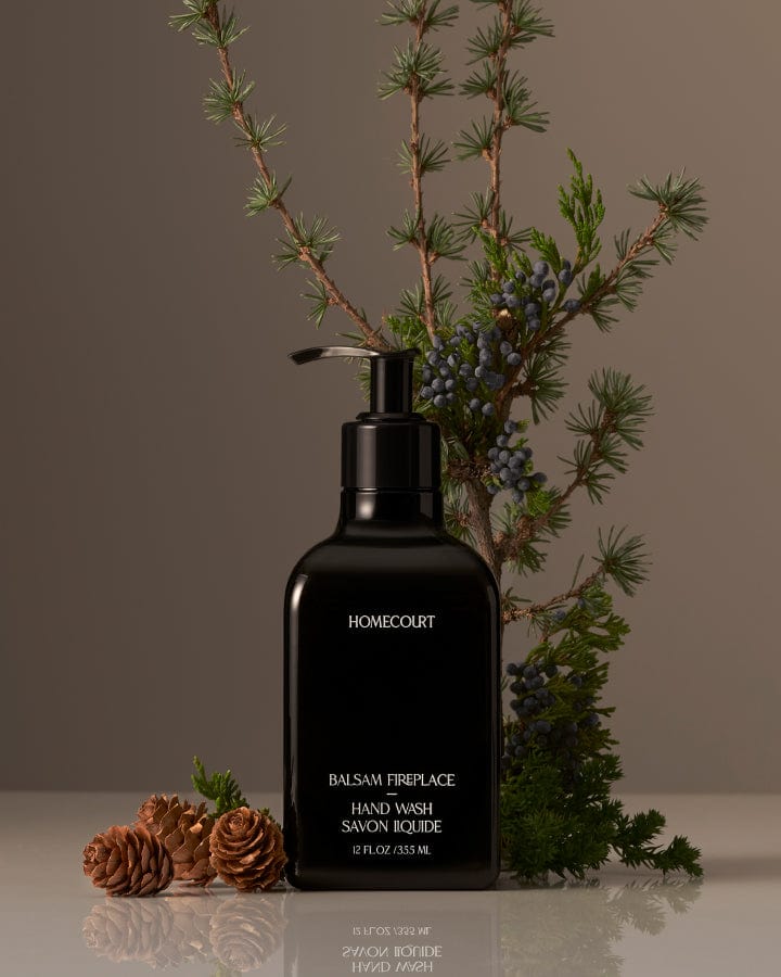 Black pump bottle of award-winning Homecourt Balsam Fireplace Hand Wash with balsam fir branches and pine cones around it.