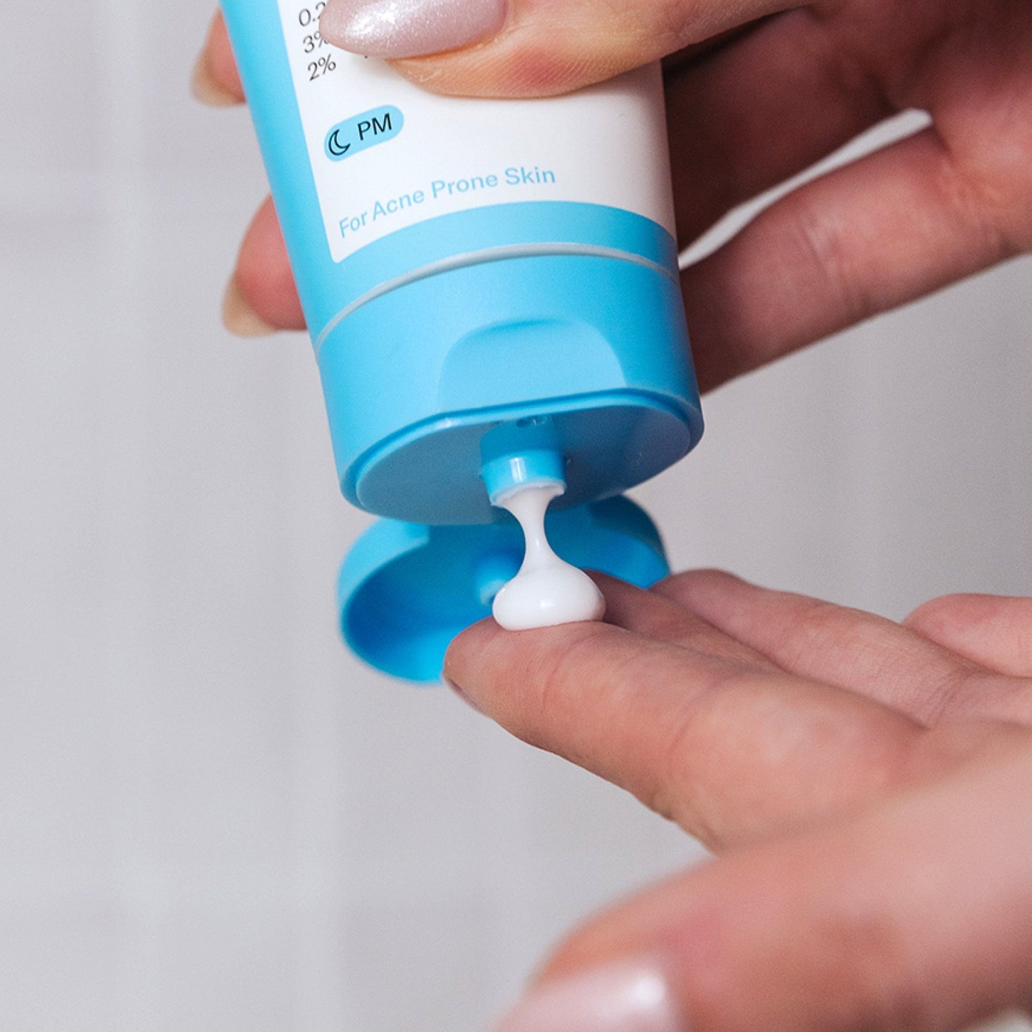 Hand applying Geologie Skin Repair Moisturizer from the blue and white tube on a light gray background.
