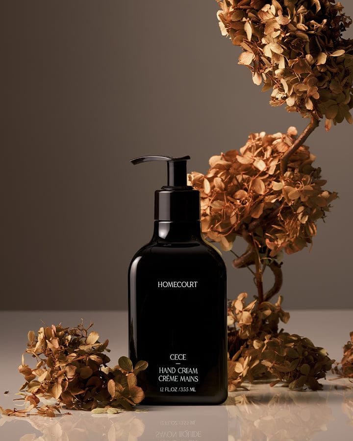 Black Homecourt Hand Cream bottle labeled with dried Cece flowers on a reflective surface.