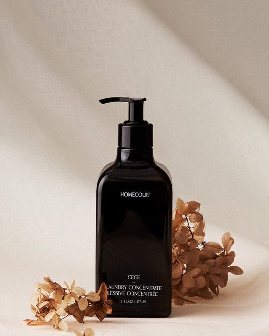 Black bottle of Homecourt plant-based 10X Laundry Concentrate with dried Cece flowers on a beige background.