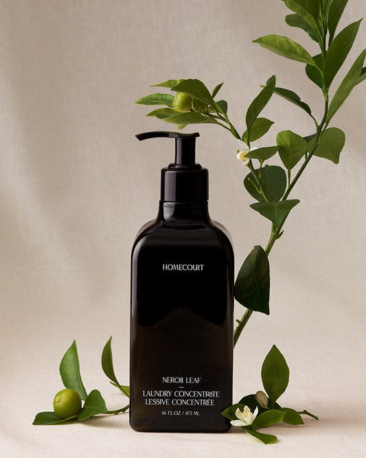 Black bottle of Homecourt plant-based 10X Laundry Concentrate with Neroli leaves and flower on a beige background.