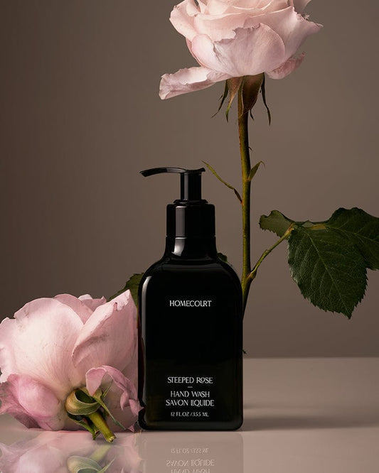 Black pump bottle of award-winning Homecourt Steeped Rose Hand Wash with pink roses on a reflective surface.