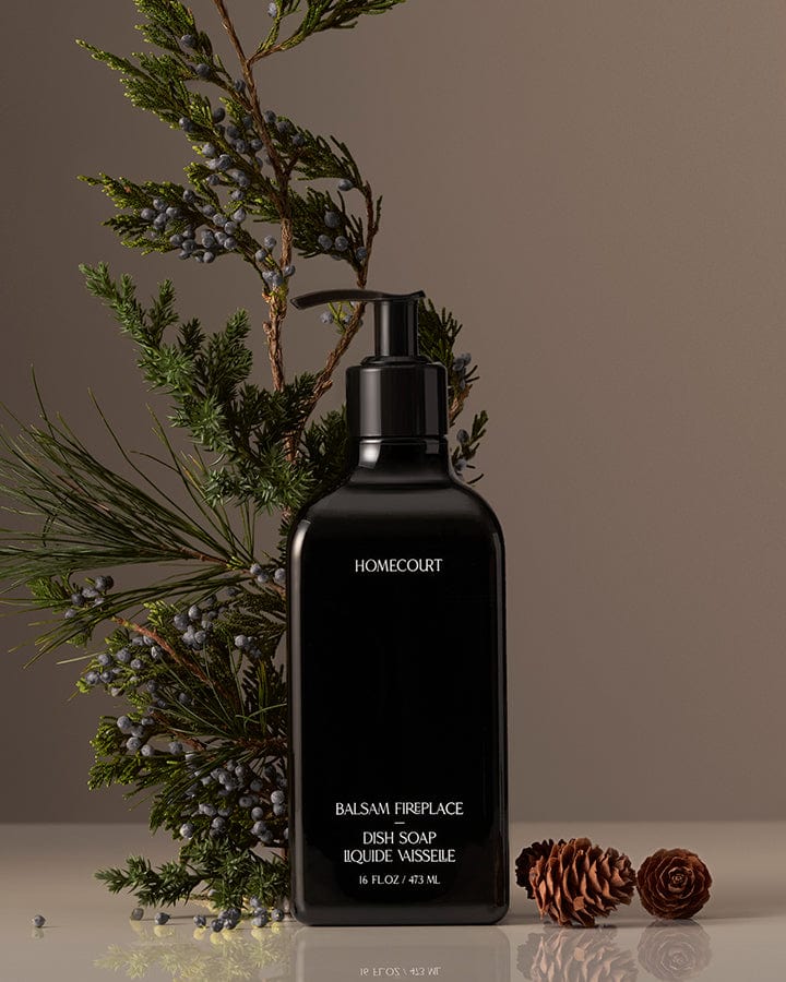 Black bottle of Homecourt Award-Winning Dish Soap with Balsam branches and pinecones on a neutral background.