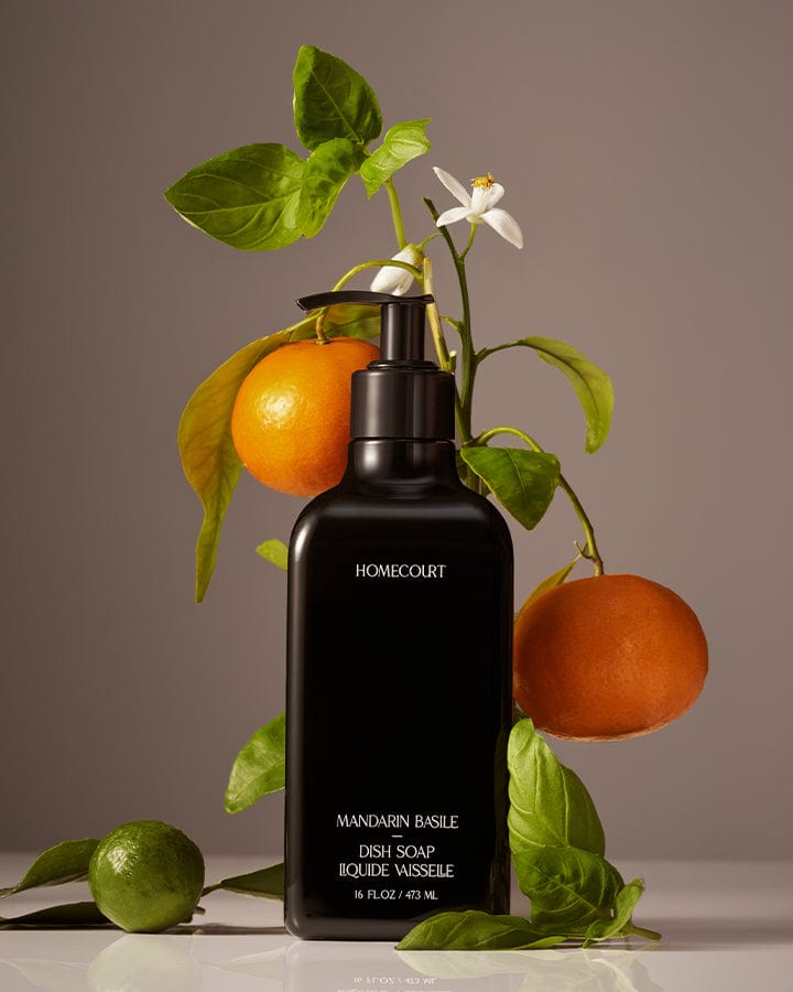 Black bottle of Homecourt Mandarin Basil dish soap with mandarin oranges and basil leaves on a neutral background.
