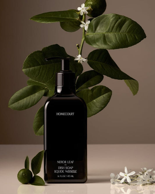 Black bottle of Homecourt Award-Winning Dish Soap with green leaves and white flowers on a neutral background.