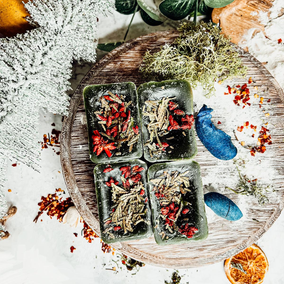 Four Cedar Berry XL green wax melts with dried herbs on a wooden board with decorative winter elements.