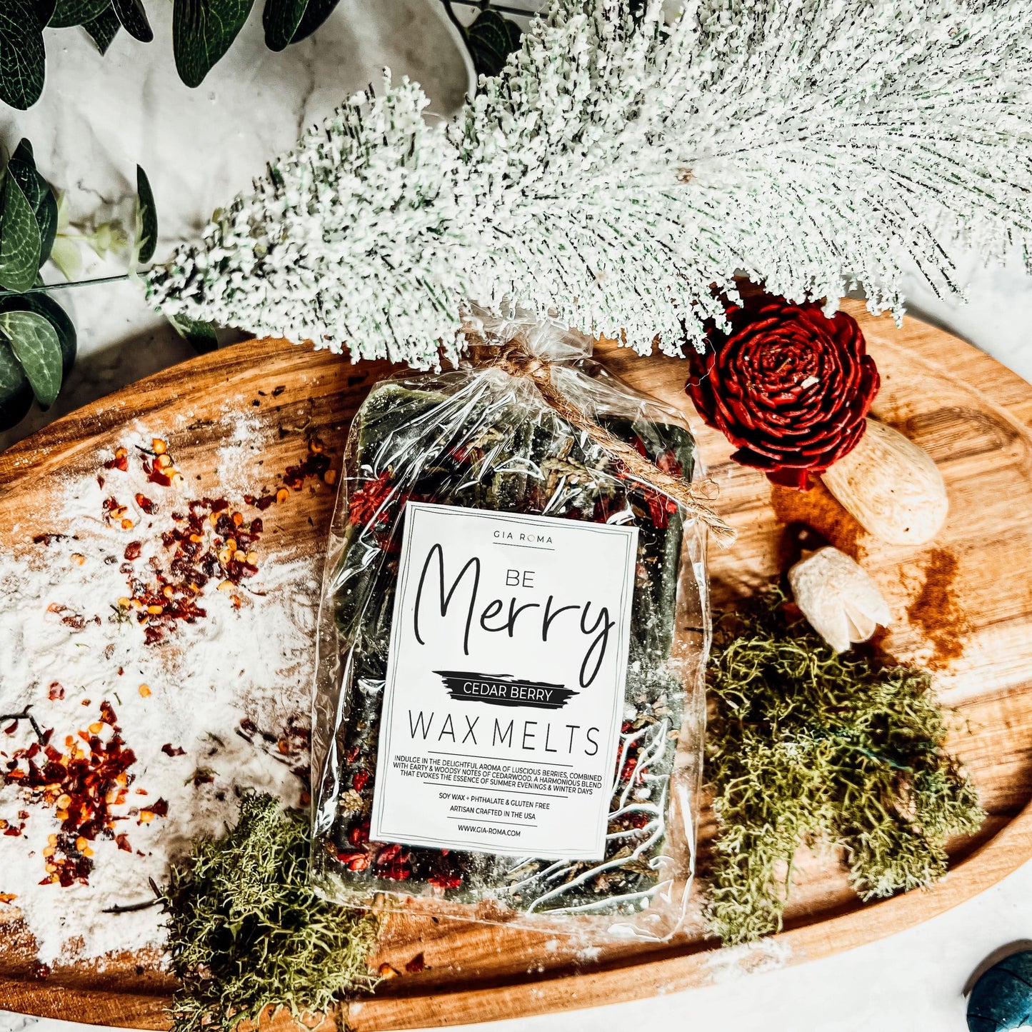 Packaged Cedar Berry XL wax melts labeled 'Be Merry' on a decorative wooden board with a winter tree and greenery.