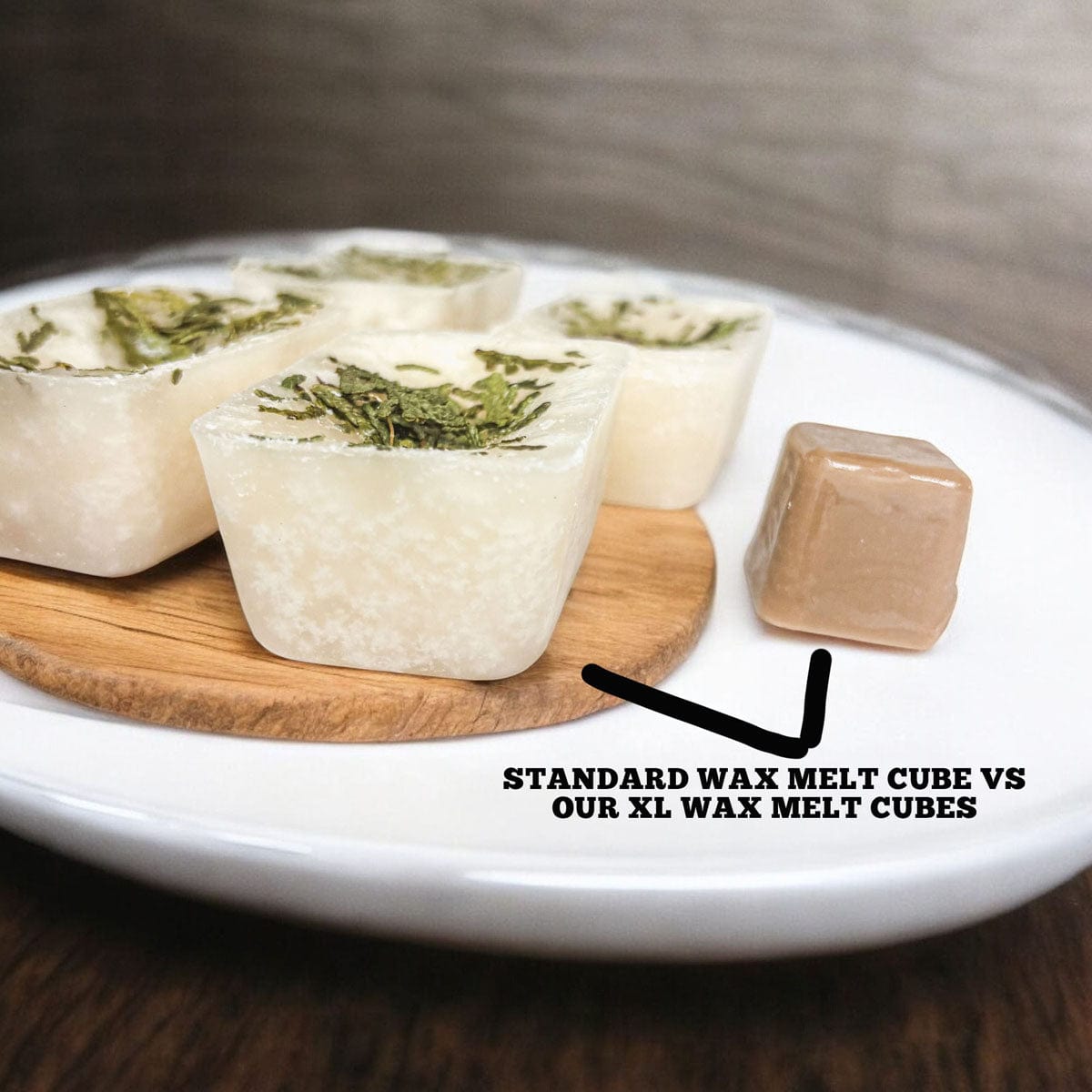 Comparison of standard wax melt cube and Christmas Tree XL wax melt cube on a wooden coaster with a white plate.