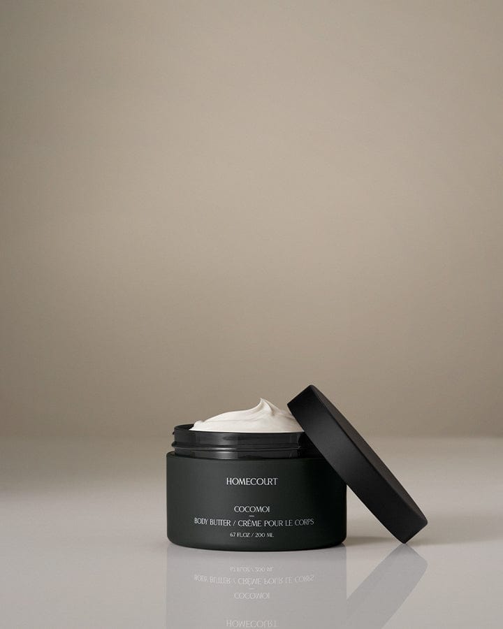 Black jar of Homecourt Indulgent Body Butter with the lid off on a beige background.