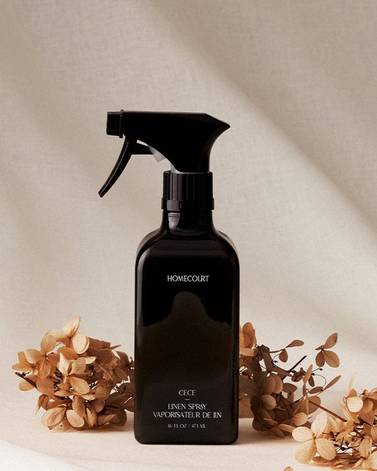 Black spray bottle of Homecourt Natural Linen Spray on a neutral background with dried Cece flowers.