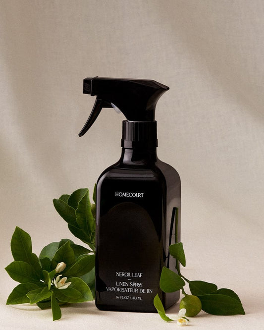 Black spray bottle of Homecourt Natural Linen Spray with Neroli branches on a neutral background.