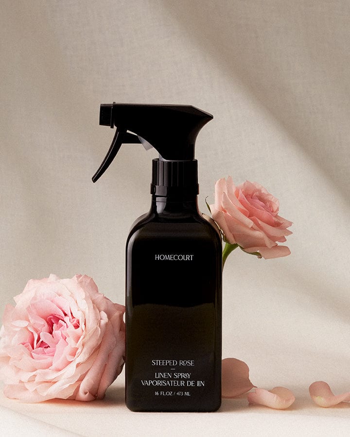 Black spray bottle of Homecourt Natural Linen Spray with pink roses on a neutral background.