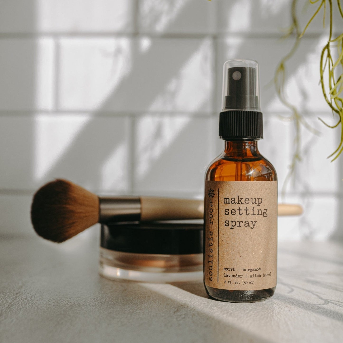 Makeup setting spray bottle with a brush and jar on a light surface.