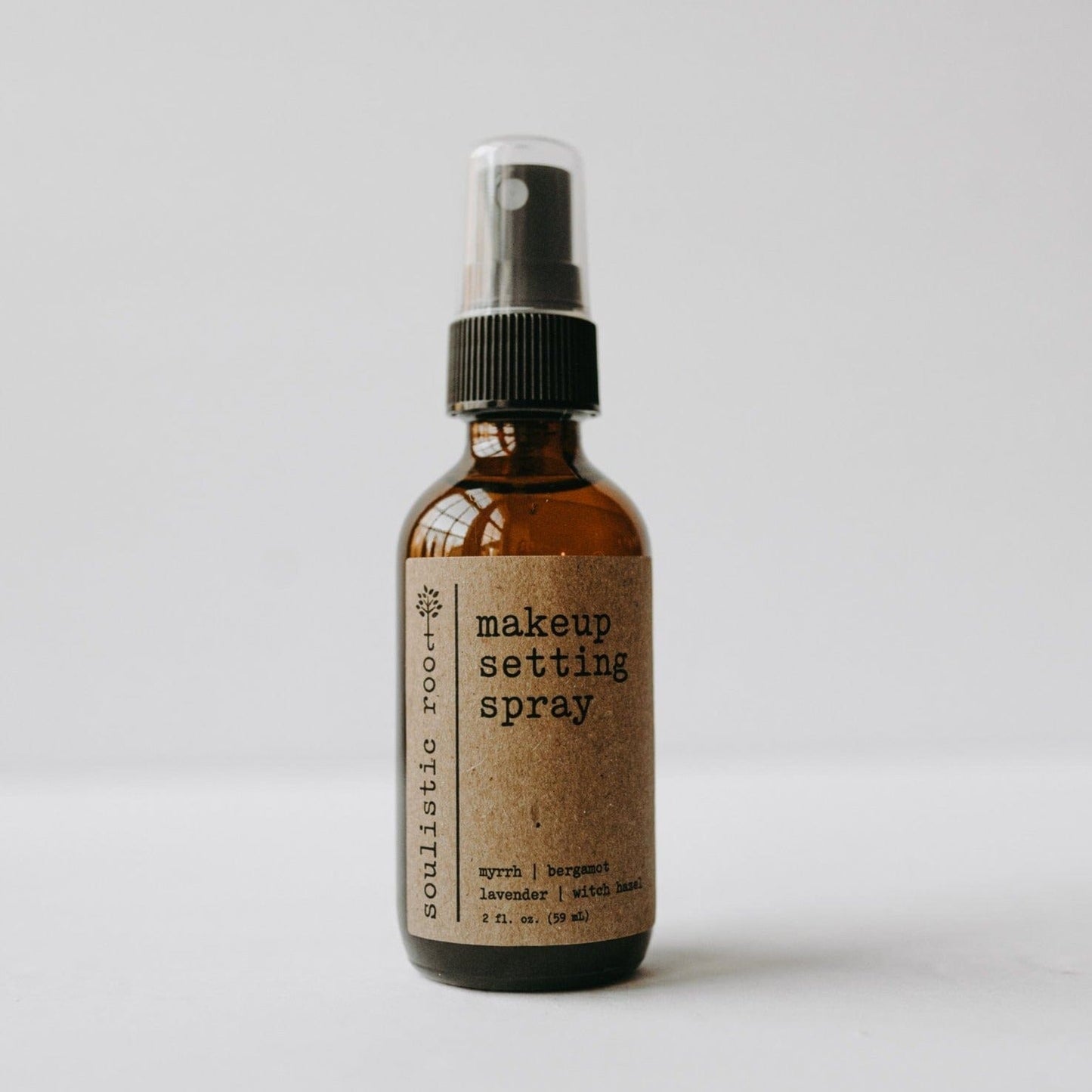 Makeup setting spray bottle with a brown label on a light gray background.