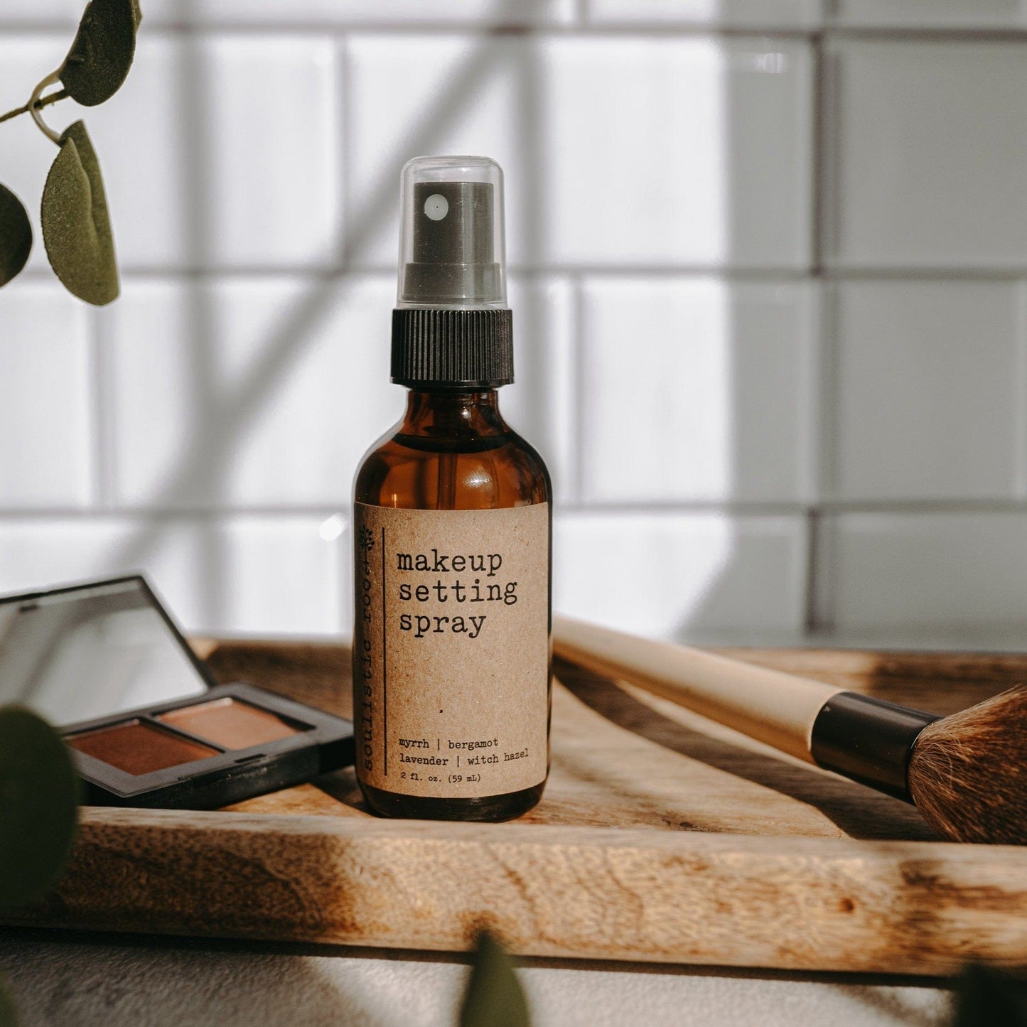 Makeup setting spray bottle on a wooden surface with blush in a bathroom with a plant and blurred background.