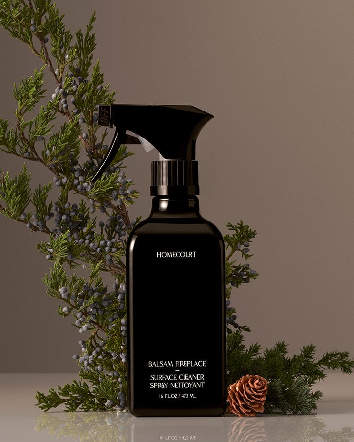 Black spray bottle of Homecourt Natural Surface Cleaner with Balsam Fir greenery and pinecones in the background.