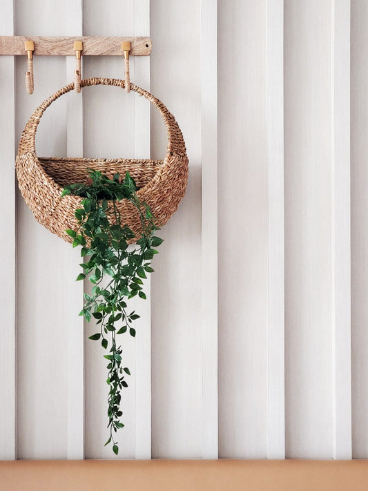 Savar Seagrass Wall Hanging Basket with hanging plan inside against a striped wall.