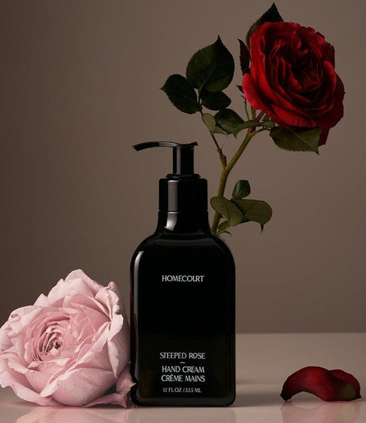 Black Homecourt Rose Hand Cream bottle with roses around it on a reflective surface.