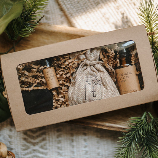 Therapeutic Travel Gift Set with bottles and a pouch in a brown box, surrounded by greenery.