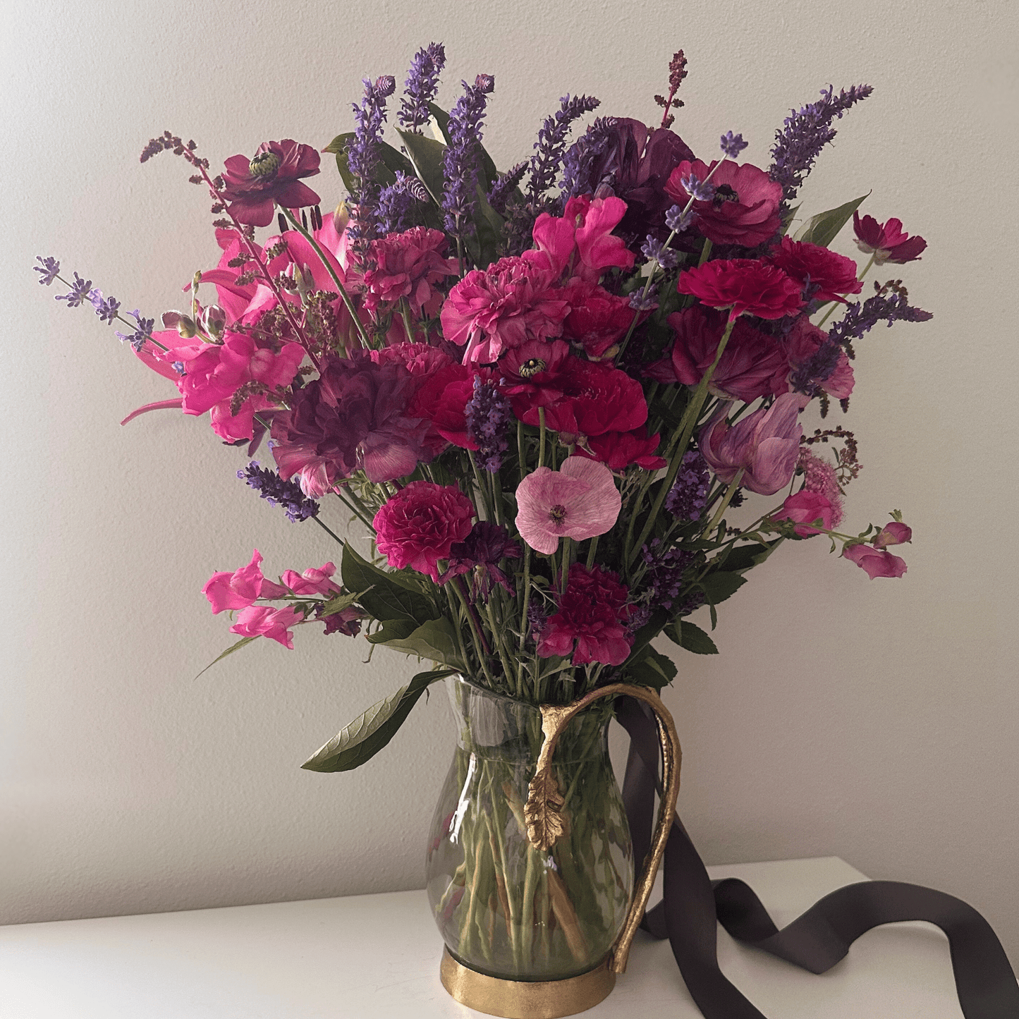 Dark purple and pink ranunculus, anemones, poppies, snapdragons and more arranged in a gold vase by Little Mountain Flowers