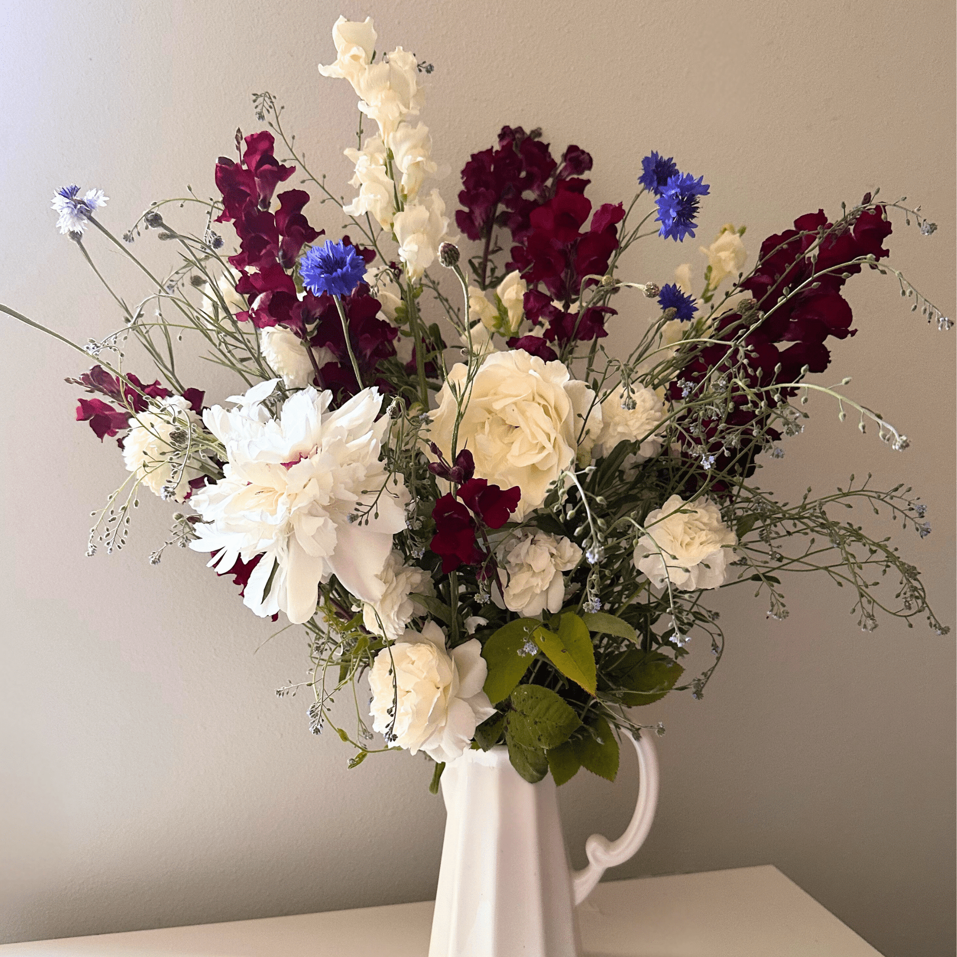 A 4th of July display of Peonies, roses, snapdragons, and blue bachelor button grown & arranged by Little Mountain Flowers