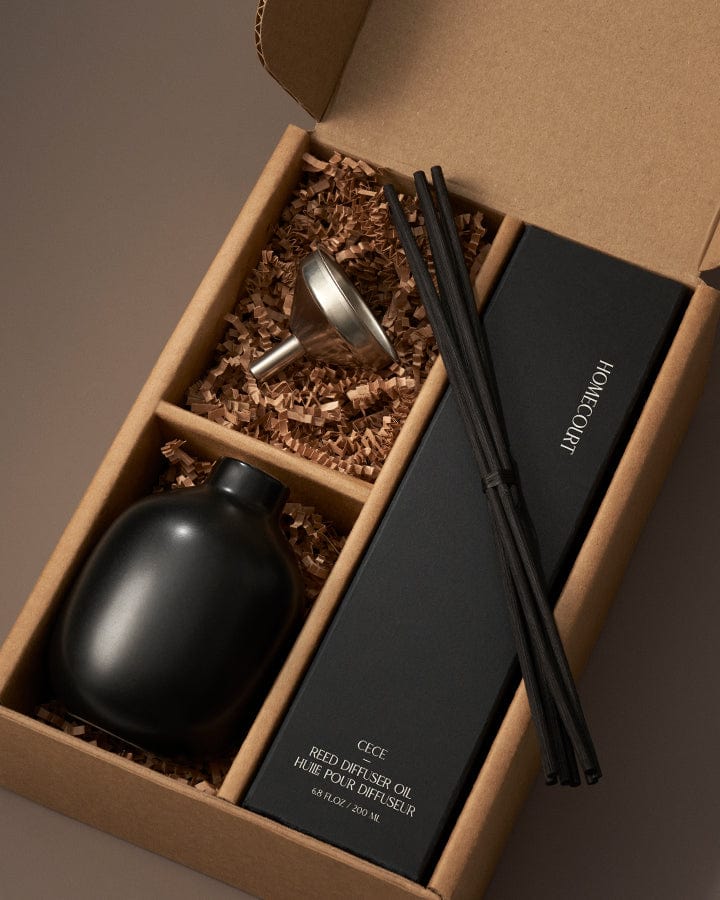 Zen Reed Diffuser set with black bottle, black box, and black sticks in a brown box on a brown background