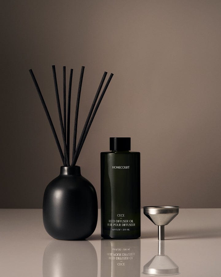 Black Homecourt diffuser bottle with reeds and a small metallic container on a reflective surface with a brown background